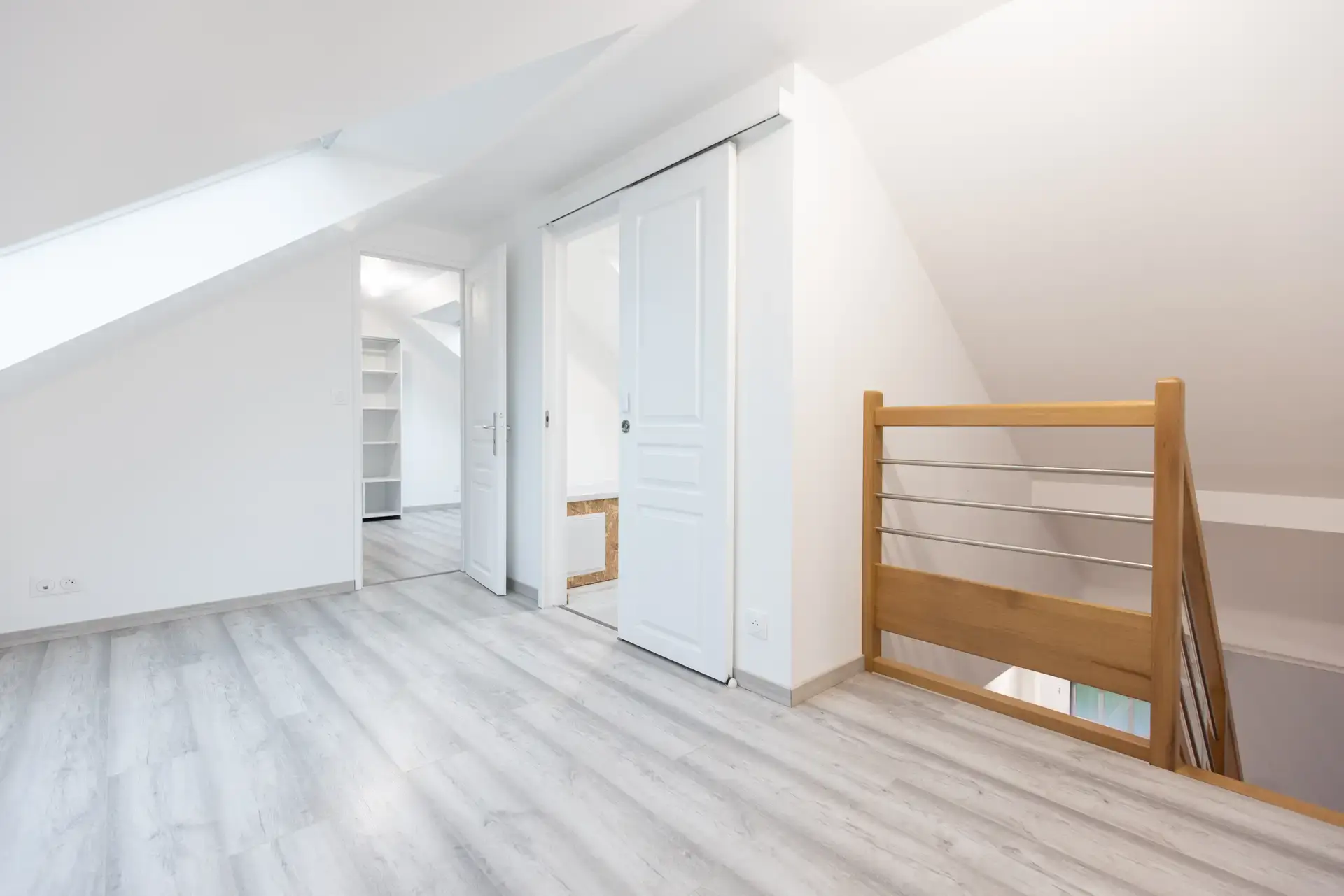 Pièce aménagée sous combles, sol clair et trémie d'escalier en bois